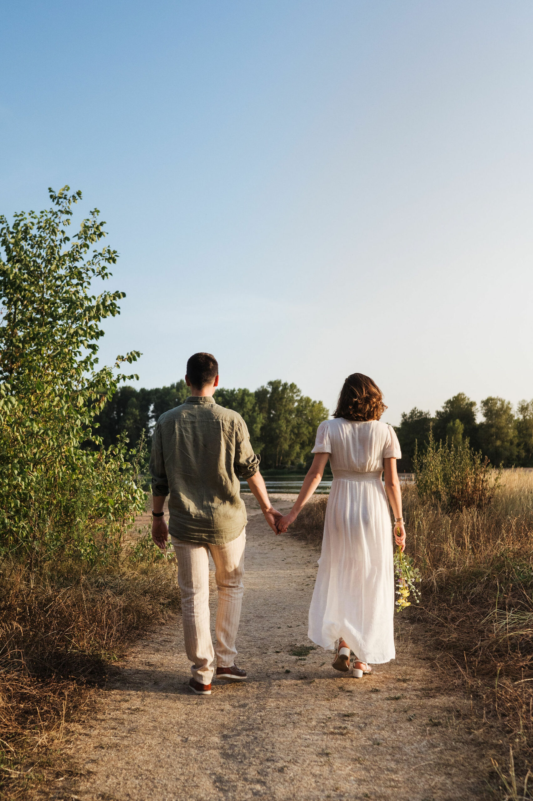 Couple enlacé de dos marchant au bord de l'eau à Combleux, séance photo naturelle avant mariage