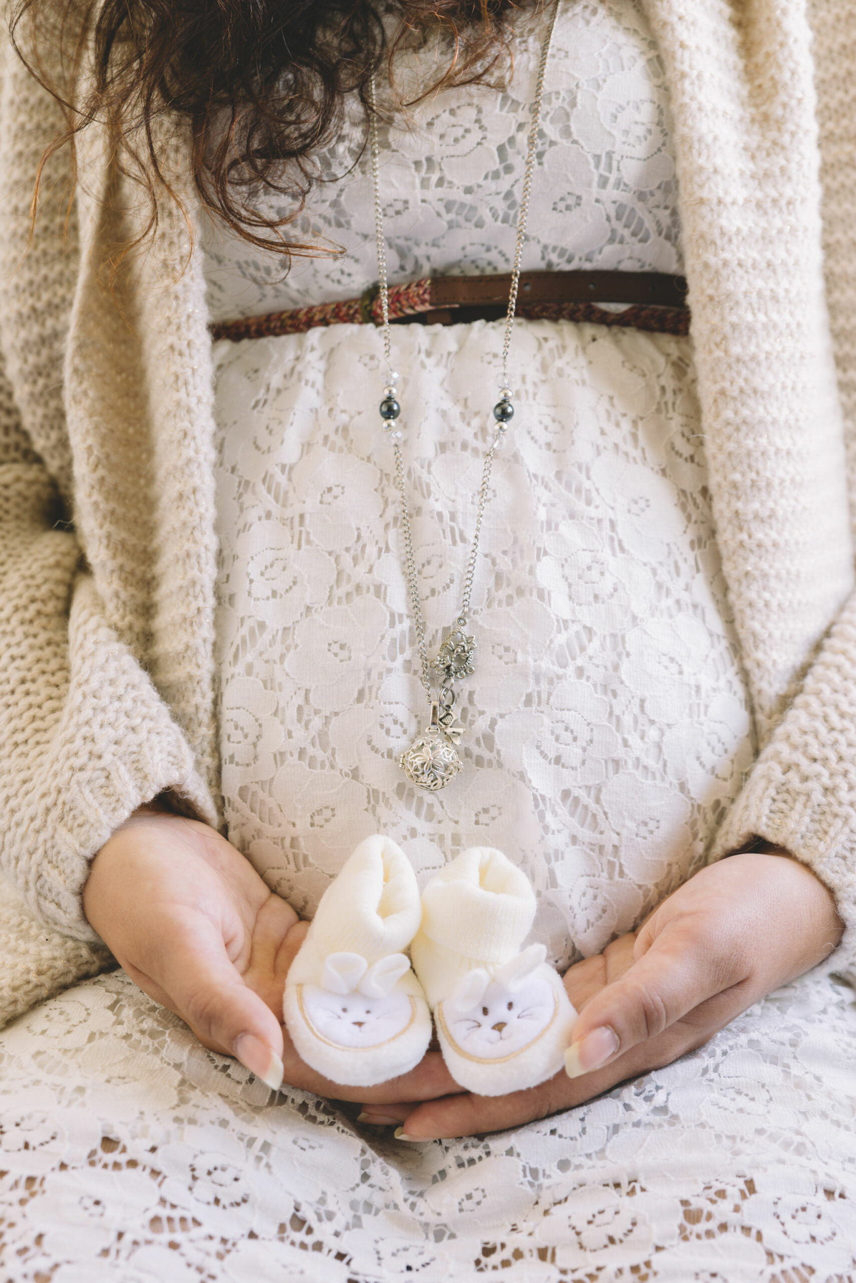 Mains d'une future maman tenant de petits chaussons de bébé sur son ventre