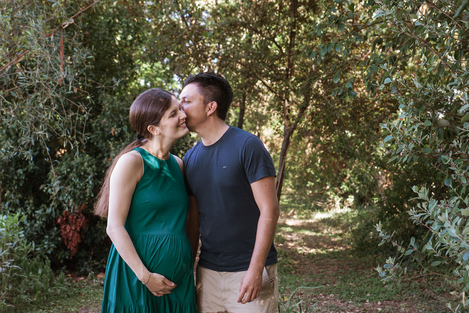Futur papa embrassant sa compagne enceinte sur la joue, en pleine nature