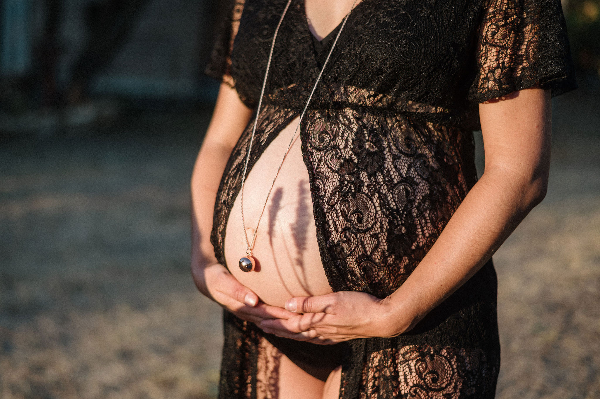 Gros plan sur le ventre d'une future maman en robe de dentelle noire, au coucher du soleil