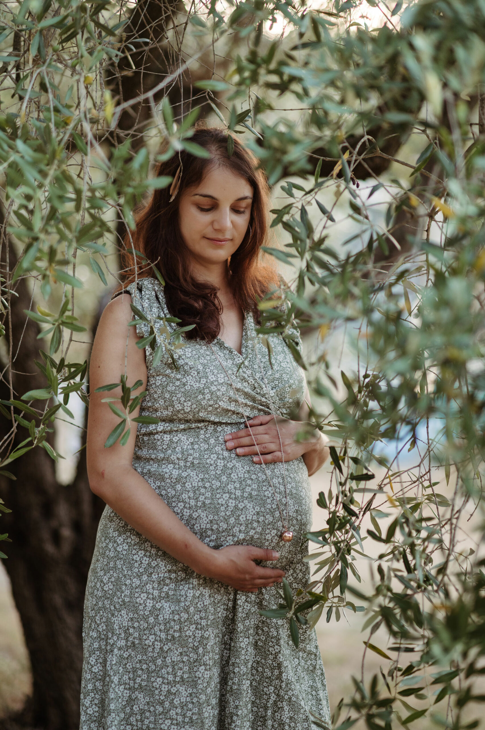 Future maman en robe fleurie entre les branches d'un olivier